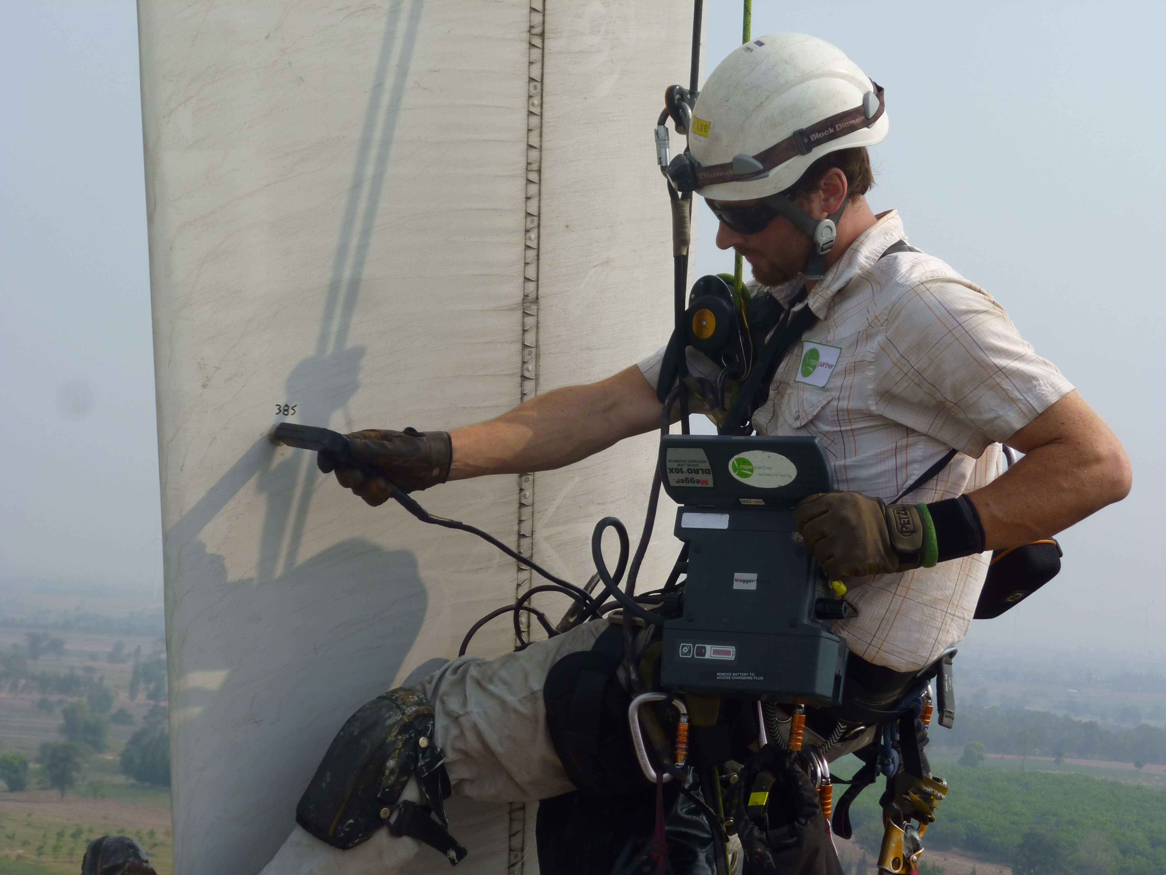 A wind tech, suited up in fall-protection gear, safely rappels down to a turbine blade to test the asset’s lightning-protection system during an onsite O&M visit
